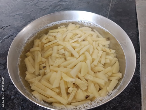 Foto The image shows raw, cut potatoes soaking in water, which is a common preparation step for making French fries