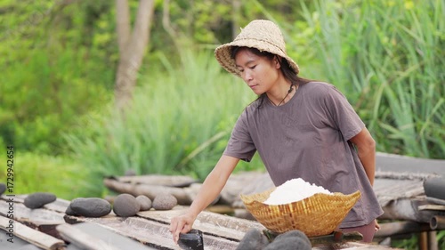 farmer harvesting natural crystalized sea salt from coconut trunks in bali indonesia, traditional hat, slow motion