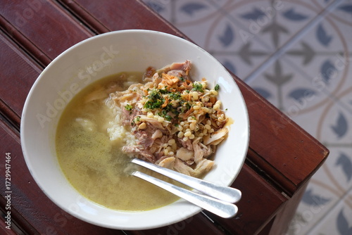 Chicken soto in a white bowl on a wooden table. Indonesian food. soto ayam Kediri. turmeric chicken clear soup.