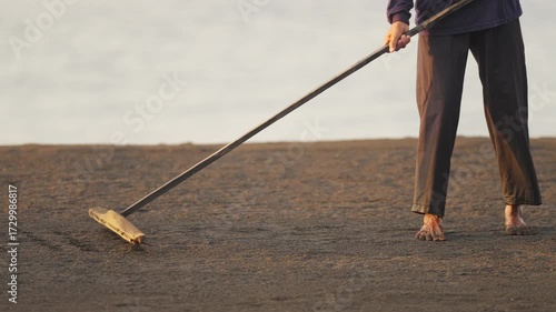 Traditional salt farmer in bali preparing sand for harvesting, slow motion