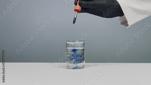 Photos Dropper pipette releasing blue dye into clear water inside glass beaker on labor