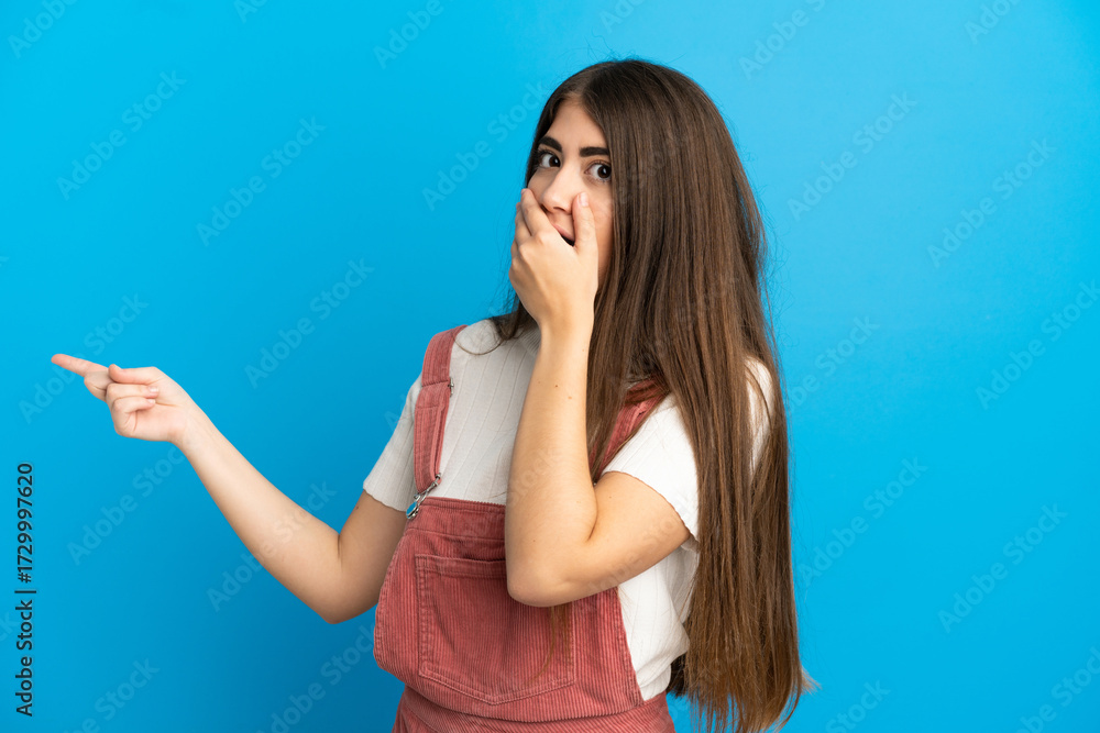 Fototapeta premium Young caucasian woman isolated on blue background with surprise expression while pointing side