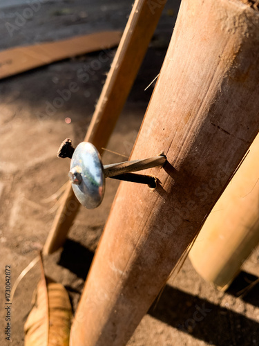 Detail of a large, silver metal nail with washer driven into a light brown bamboo pole or stake. Construction hardware secures the wood, creating a contrast between rustic material and industrial fast