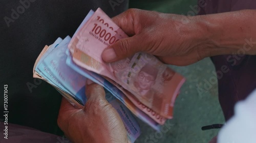 Close-up of workers’ hands holding and counting Indonesian rupiah banknotes, shifting the money between fingers.