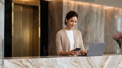 Woman at Reception Desk Working on Laptop and Using Mobile Phone