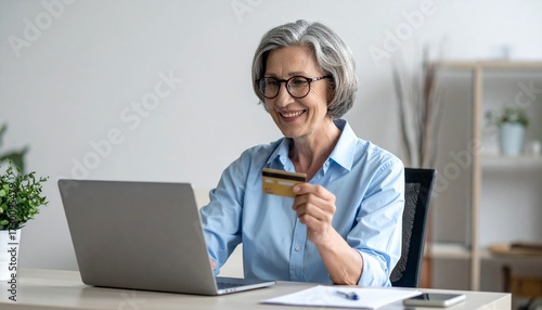 Elderly woman sitting at a desk, looking at a laptop. Holding a credit card ready to make an online payment