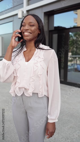 Vertical video of smiling African american businesswoman talking on the phone outside office building
