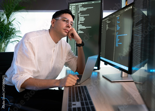 Tired programmer working at a modern desk surrounded by multiple monitor during a busy day in a bright office space