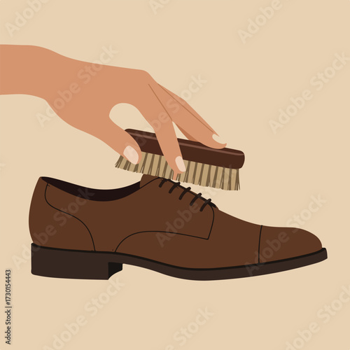 Hand brushing a brown leather dress shoe with a brown brush, tan background