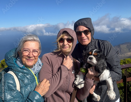 Joyful group of senior friends with a small dog enjoying trekking in mountain in a sunny windy day, four mature people looking at camera smiling. Sport, freedom, healthy lifestyle concept