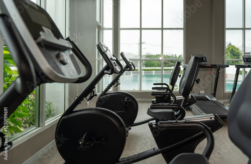 Interior view of a fitness center featuring several exercise machine, including stationary bike and treadmill, with large window offering a view of an outdoor pool.