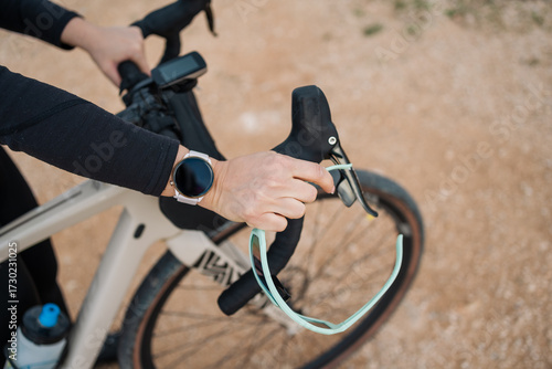 Young woman cyclist wearing smartwatch holds gravel bike handlebars