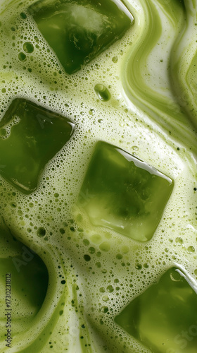 Close-up of iced matcha latte with ice cubes and creamy foam. Bright green and creamy swirls create a textured, calming background, perfect for food blogs, wellness, advertising, and design.

