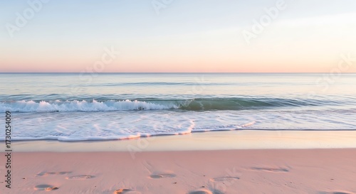 Gentle ocean waves wash ashore on a sandy beach at sunrise