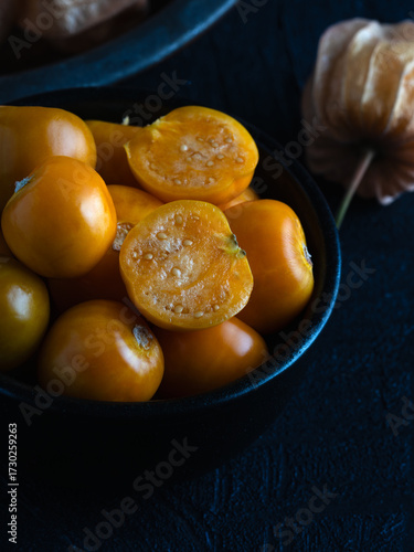 Close-up of fresh golden berries, also known as physalis or ground cherries, in a black bowl on a dark textured background.