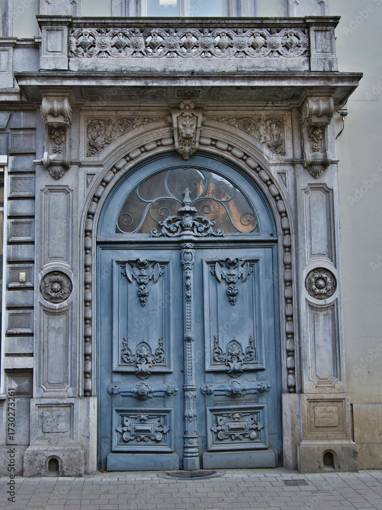 Obraz premium Rustic Blue Door on a Historic Facade - An ornate, rustic blue door with intricate carvings and an arched transom on a weathered stone building in Ghent, Belgium.