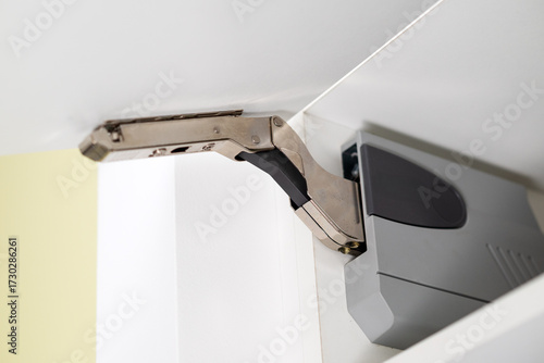 A closeup shot of a modern kitchen cabinet hinge mechanism, showing a gas lift strut in an open position.