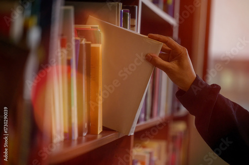 Hand picking book from library bookshelf for reading and education concept, symbolizing knowledge, education, learning, research, study, literature, academic resources in a quiet study environment