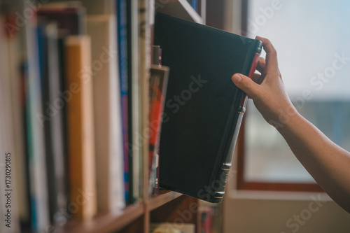Hand picking book from library bookshelf for reading and education concept, symbolizing knowledge, education, learning, research, study, literature, academic resources in a quiet study environment