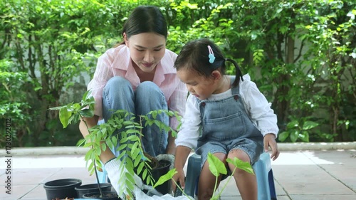 Family hobby and relationships and home activities : Mother and her adorable young daughter planted potted trees together to decorate their garden, making it shady and inviting.