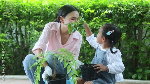 Family hobby and relationships and home activities : Mother and her adorable young daughter planted potted trees together to decorate their garden, making it shady and inviting.