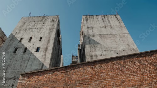 Wallpaper Mural Two unfinished concrete towers abutting a weathered brick wall against a clear sky Torontodigital.ca