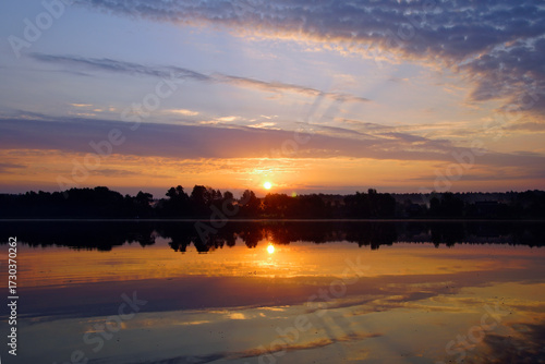 Beautiful moments of sunrise. Shot from the surface of the lake, the shore and trees against the beautiful sky. Morning fog. Reflection on the surface of the water.