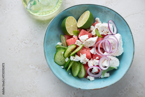 Turquoise bowl with watermelon and feta cheese salad, horizontal shot on a light-beige stone background, high angle view