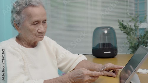 An elderly Asian woman use a credit card to pay for goods via tablet, online shopping, contactless payment