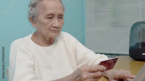 An elderly Asian woman use a credit card to pay for goods via tablet, online shopping, contactless payment