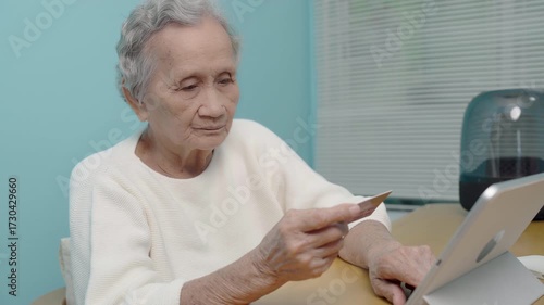 An elderly Asian woman use a credit card to pay for goods via tablet, online shopping, contactless payment