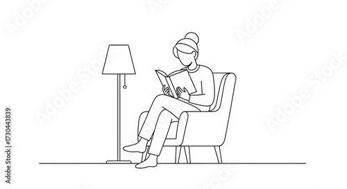 Woman reading a book in an armchair next to a lamp.