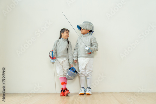 ฺAsian brother and sister with fencing sport uniform stand beside  also look at face and smile to relax during practice for competition.
