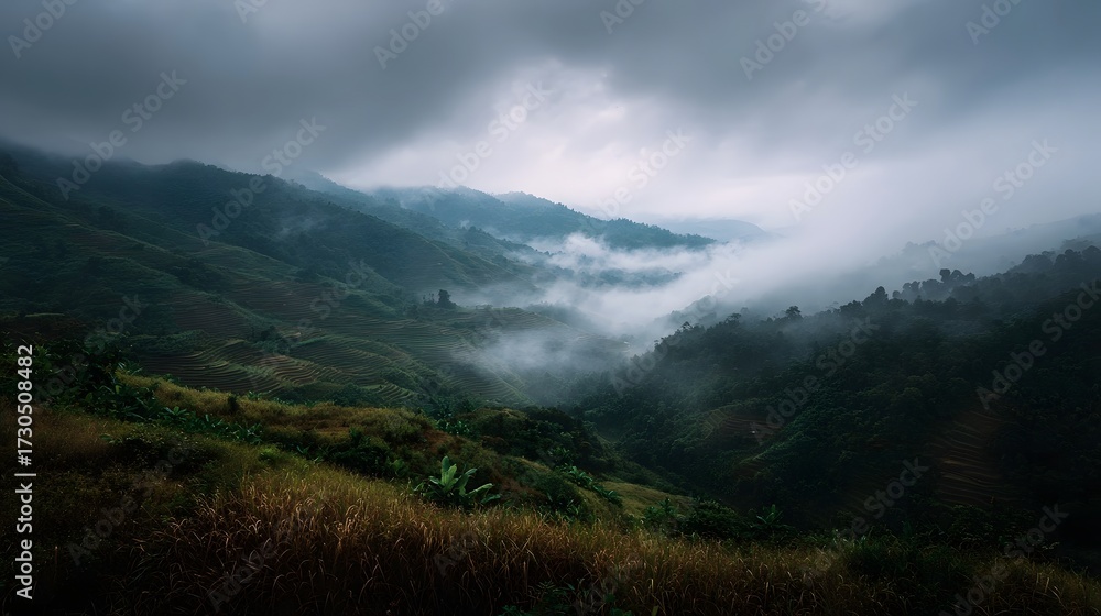 Fototapeta premium Moody mountain landscape shrouded in mist with layered green slopes and dramatic clouds