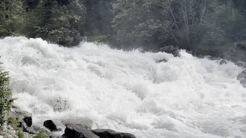 A fast-flowing mountain river with clear water crashing over large rocks and boulders. Large water splashes. Clean and natural river water in a rural area