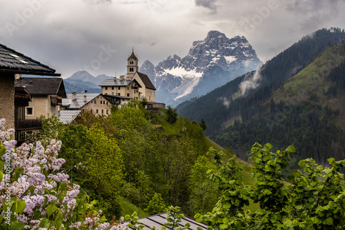 Church perched on steep sided hill in Colle Santa Lucia village with dramatic Dolomites peak of Monte Pelmo rising from forested valleys