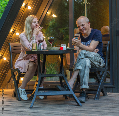 A man and woman drinking wine on the veranda of a cabin in the woods