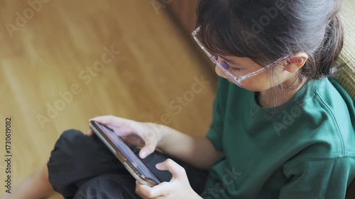Asian kid, a young girl, is playing a game on her mobile phone at home. This shows child interacting with smartphone technology, highlighting focused entertainment and modern childhood.
