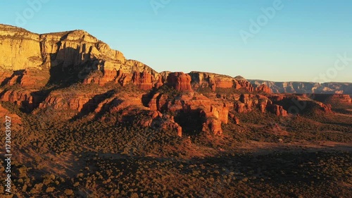 Aerial drone footage of Bear Mountain and red rock formations at sunset in Sedona, Arizona, with warm golden light and slow dolly-in camera motion over the dramatic desert landscape.