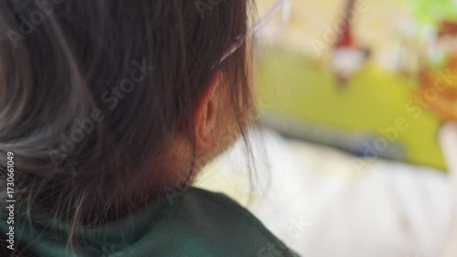 Close-up of an Asian girl's face, playing a game on a digital tablet. Selective focus shot shows her concentration and interaction with the screen, reflecting modern childhood and technology.