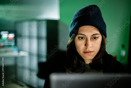 Hacker breaking into a secure network, programming malicious code on her computer in a dark room