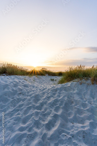 Wunderschöner Sonnenuntergang hinter mit Gras bewachsenen Dünen am Meer