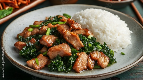 Stir-fried pork or chicken with kale and rice on a light plate