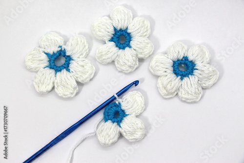 A flower with six white petals and a blue center crocheted on a white background.