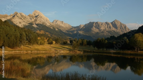 A serene mountain landscape at sunrise or sunset with calm water reflecting lush green trees and rugged mountains under 