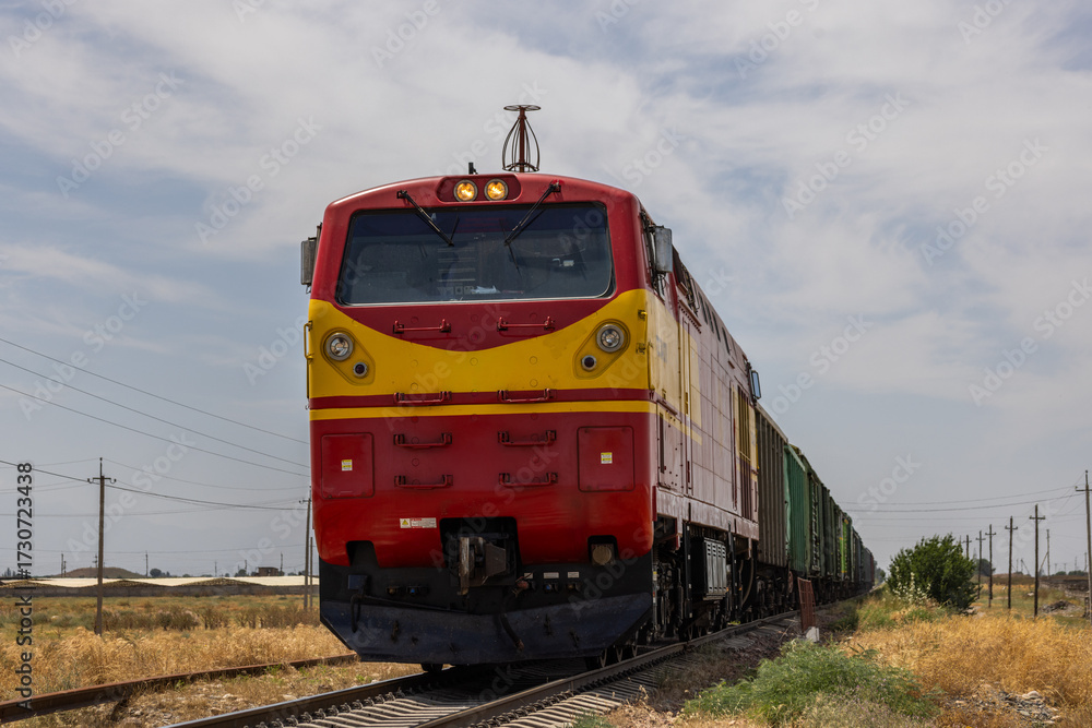 Fototapeta premium Freight train moving through serene rural landscape during daytime in Kyrgyzstan