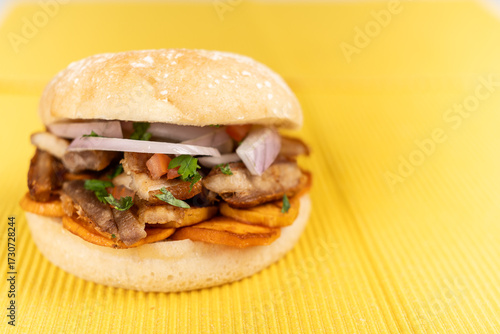 Peruvian pork and sweet potato sandwich served on a yellow background.