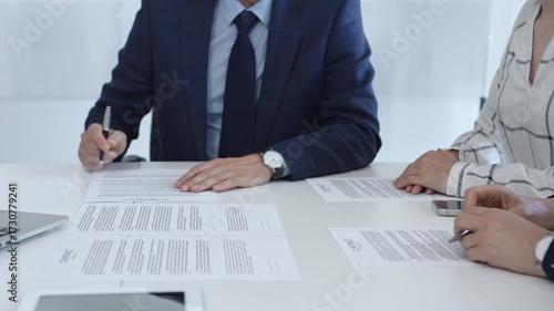 Professional businessman wearing tailored suit signing contract at sleek desk, sealing business agreement with collaborative partners in contemporary workspace