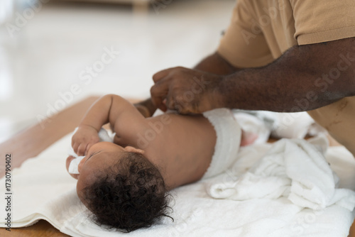 African American father wearing newborn baby diaper on white towel after taking shower. Father changing newborn baby diaper at home