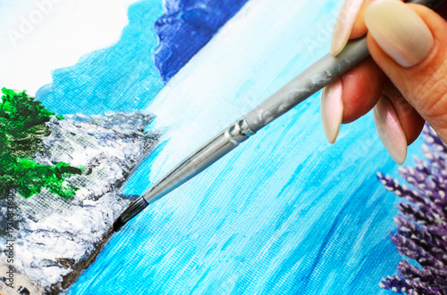 Artist hand with brush adding white strokes on rocky seascape